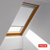 A VELUX skylight window with a white roller blind partially covering it, showing sunlight casting shadows on the white walls. Produktbild-Vorschau