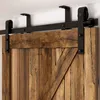 A close-up view of a rustic wooden sliding barn door with a black metal track and roller system. Produktbild-Vorschau