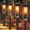 Four solar garden lights are illuminated in a garden bed filled with pink and white flowers. Produktbild-Vorschau