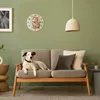 A dog is lying on a sofa in a living room, with a cat clock on the wall. Produktbild-Vorschau