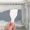 A hand is holding a white ice scraper inside a freezer, chipping away at a large chunk of ice. Produktbild-Vorschau