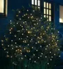 A bush decorated with warm white LED lights at night, with a house in the background. Produktbild-Vorschau