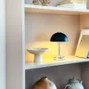 A black and chrome table lamp sits on a shelf next to a decorative bowl. Produktbild-Vorschau