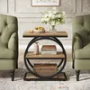 A wooden side table with a round metal frame is placed between two green armchairs, decorated with a vase of white flowers and a bowl of fruit on top. Anteprima dell’immagine prodotto