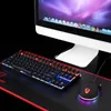 A gaming keyboard and mouse set with RGB lighting, placed on a black mousepad with red trim, in front of a computer monitor. Produktbild-Vorschau