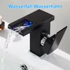 A black waterfall faucet with blue LED lighting is shown in a bathroom sink, with water flowing. Produktbild-Vorschau