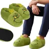 A person wearing Grinch-themed slippers, with a pair of the slippers shown separately. Produktbild-Vorschau