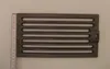 A cast iron grate is placed on a light gray background with a ruler to its left. Náhled obrázku produktu
