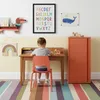 A child sits at a desk in a colorful room, drawing. Voir les images du produit