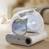 A futuristic automatic cat litter box with a transparent dome, showing internal workings and airflow, placed on a wooden floor next to a white cat. The background is a blurred living room setting with a sofa. Anteprima dell’immagine prodotto