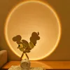 A lamp casting a sunset-like glow on a wall, with a vase of greenery and a small white device in the foreground. Produktbild-Vorschau