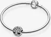 A silver Pandora bracelet with two charms, one a spherical charm with the Pandora logo and the other an openwork charm shaped like a tree. Podgląd zdjęcia produktu