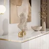 A white high-gloss dresser with gold trim, decorated with a bust, a bowl, and a vase with dried branches. Produktbild-Vorschau