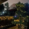 A nighttime outdoor scene with decorative lights on a fence and a tree, with a building in the background. Náhled obrázku produktu