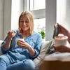 A woman is sitting on a couch and eating ice cream from a container. Produktbild-Vorschau