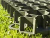 A close-up view of a black plastic grid system laid over green grass. Produktbild-Vorschau