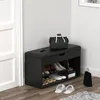 A black shoe bench with storage is placed in a hallway next to a white door. There is a black bag on top of the bench and shoes are stored inside the shelves below. White slippers are on the floor in front of the bench. Produktbild-Vorschau