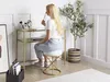 A woman is applying makeup while sitting on a stool in front of a vanity table. Produktbild-Vorschau