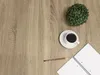 A top-down view of a wooden desk with a small potted plant, a cup of coffee, a notebook, and a pencil. Produktbild-Vorschau