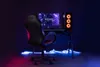 A gaming chair and desk setup with a computer and monitor, illuminated by neon lights. Produktbild-Vorschau