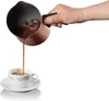 A hand is pouring coffee from a bronze coffee pot into a white cup. Produktbild-Vorschau