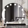 A vanity mirror with lights is placed on a dresser with makeup products in front of it, and a bed in the background. Náhled obrázku produktu