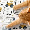 An orange cat is lying on a patterned surface with construction vehicle illustrations. Náhled obrázku produktu