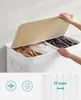 A person is opening the lid of a white laundry basket with three compartments, revealing folded clothes inside. Produktbild-Vorschau