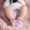 A baby's legs are resting on a pink knitted blanket, with a pink jar of cream placed near their feet. Anteprima dell’immagine prodotto