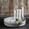 A gray candle holder with four white candles and some small white flowers. Produktbild-Vorschau