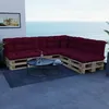 A sectional sofa made of wooden pallets with dark red cushions is placed on a balcony overlooking the ocean. Voir les images du produit