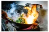 A person cooking with a wok over an open flame. Produktbild-Vorschau