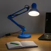 A blue desk lamp illuminates a notebook and pen on a wooden desk, with a laptop in the background. Náhľad obrázku produktu