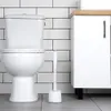 A white toilet brush with a stand is placed next to a white toilet in a bathroom with white subway tiles. Podgląd zdjęcia produktu