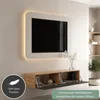 A modern TV board mounted on a wall with a TV above it, featuring open compartments and decorative elements. Produktbild-Vorschau