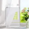 A clear, flat water bottle is placed on a surface, with a blurred background of a window and flowers. Produktbild-Vorschau