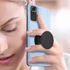 A woman is holding a light blue smartphone with a black PopSocket attached to the back. Produktbild-Vorschau