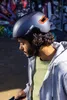 A person wearing a helmet in an urban outdoor setting with graffiti art in the background. Produktbild-Vorschau