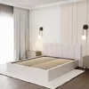 A bedroom scene featuring a bed with a slatted base and a padded headboard, a bedside table, and wall sconces. Produktbild-Vorschau