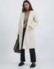 A woman models a cream-colored coat over a brown sweater and black pants, holding a dark gray tote bag. Produktbild-Vorschau