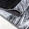 A close-up, rolled-up view of a modern abstract design rug with black, gray, and white patterns, lying on a light-colored wooden floor. Náhled obrázku produktu