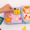 A hand is shown interacting with a soft, colorful children's book made of felt, featuring various shapes and animal figures. Produktbild-Vorschau
