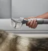 A hand holding a pet grooming attachment for a vacuum cleaner over a pet's fur. Podgląd zdjęcia produktu