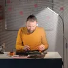 A man is working on electronic components under a bright LED floor lamp. Produktbild-Vorschau