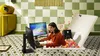A woman sits in a ball pit, playing a video game on a computer. Produktbild-Vorschau