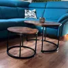 Two nesting coffee tables with wooden tops and black metal frames are placed on a wooden floor in front of a blue sectional sofa. Produktbild-Vorschau