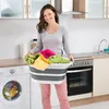 A woman is holding a laundry basket in a kitchen next to a washing machine and oven. Voir les images du produit