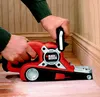 A person is using a red and black belt sander to sand a wooden floor near a baseboard. Anteprima dell’immagine prodotto