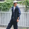 A man wearing a navy blue jacket and pants, a white t-shirt, and a white cap, standing outdoors with greenery in the background. Produktbild-Vorschau