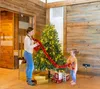 A woman and a child are decorating a Christmas tree in a room with wooden walls. Produktbild-Vorschau